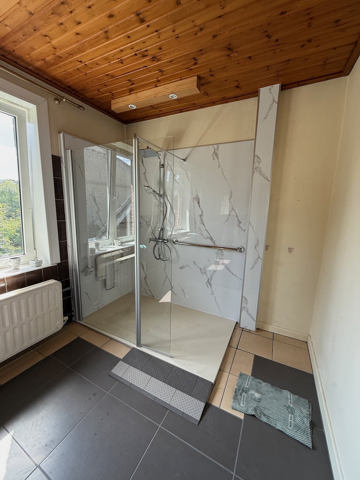 Douche senior accessible avec panneaux muraux effet marbre et barre d’appui installée dans le Hainaut