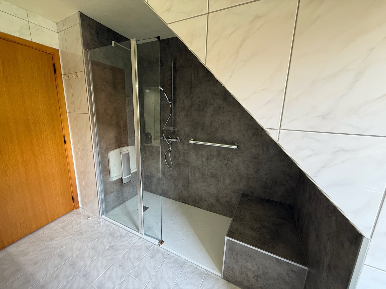 Douche senior accessible installée sous pente avec siège et barre d’appui dans le Hainaut