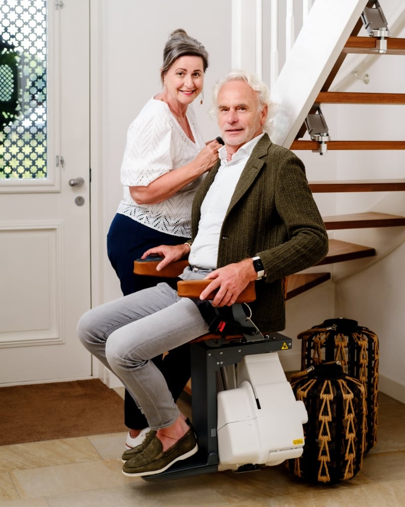 Monte-escalier tournant sur rail, senior souriant installé sur le siège — Hyseco Belgique