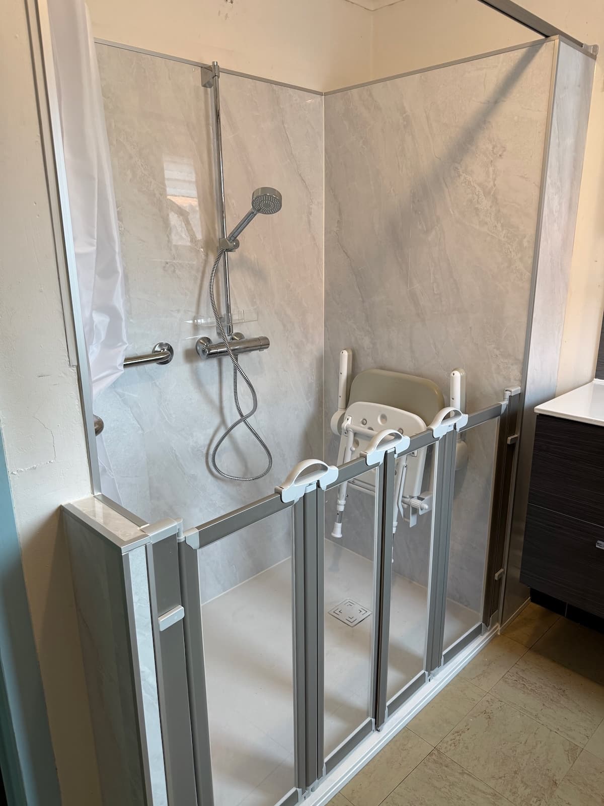 Douche senior compacte avec siège rabattable installée dans une petite salle de bain du Hainaut