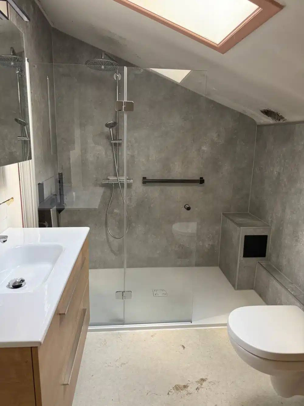Douche de plain-pied sous pente avec panneaux effet béton, barre d'appui noire et pommeau de tête, réalisation Hyseco