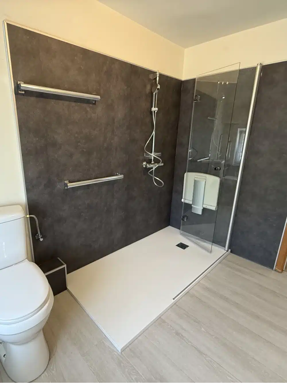 Douche de plain-pied avec panneaux anthracite, deux barres d'appui et siège escamotable, réalisation Hyseco